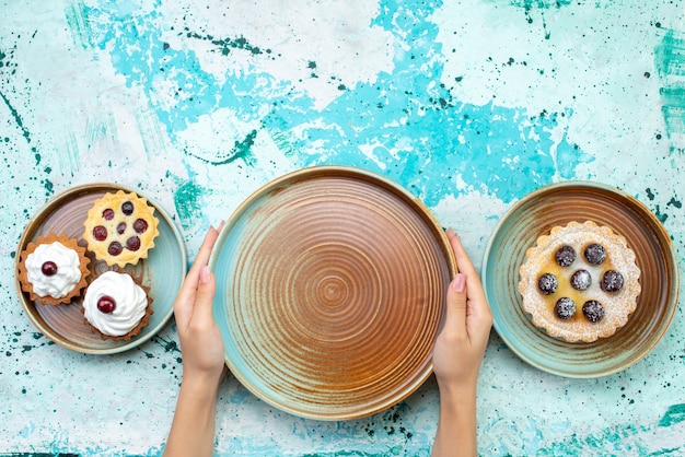 Draufsicht kleine leckere Kuchen mit Sahne und Früchten auf dem hellblauen Hintergrundkuchen süße Sahne backen Frucht