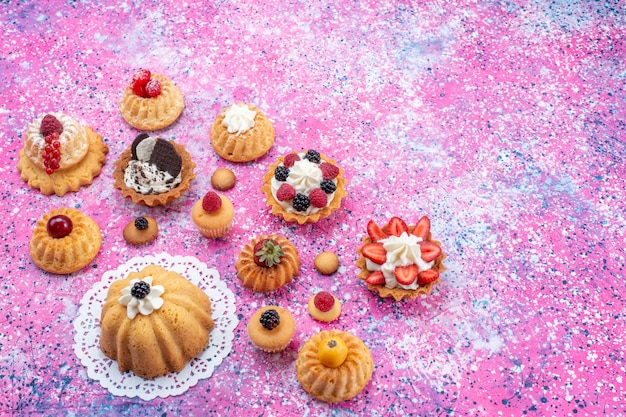 Draufsicht kleine leckere Kuchen mit Sahne zusammen mit verschiedenen Beeren auf dem hellen hellen Hintergrundkuchen-Keksbeeren-süßen Auflauf