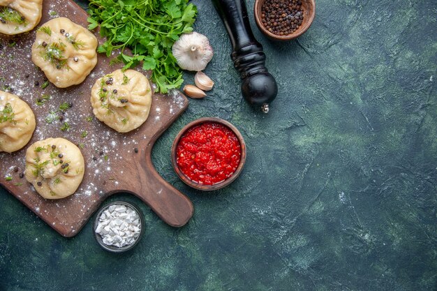 Draufsicht kleine rohe Knödel mit Tomatensauce und Grün auf dunkelblauer Hintergrundküche, die Abendessen Teiggericht Mahlzeit Fleisch kocht