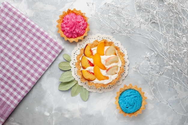 Draufsicht kleiner cremiger Kuchen mit geschnittenen Früchten und weißer Sahne zusammen mit cremigen Kuchen auf hellem Hintergrundfruchtkuchen-Kekskeks süß