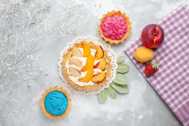 Draufsicht kleiner cremiger Kuchen mit geschnittenen Früchten und weißer Sahne zusammen mit cremigen Kuchen auf leichtem Schreibtischfruchtkuchen-Keksplätzchen