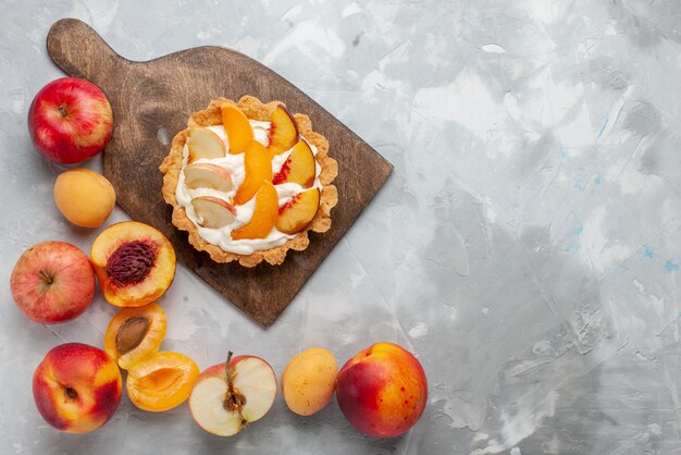 Draufsicht kleiner cremiger Kuchen mit geschnittenen Früchten und weißer Sahne zusammen mit frischen Früchten auf hellweißem Schreibtischfruchtkuchenkeks süß