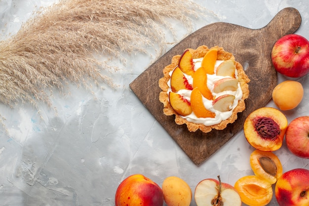 Draufsicht kleiner cremiger Kuchen mit geschnittenen Früchten und weißer Sahne zusammen mit frischen Früchten auf hellweißem Schreibtischfruchtkuchenkeks süßer Sommer