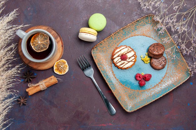 Draufsicht kleiner cremiger Kuchen mit Schokoladenkeksen und Tasse Tee auf einer dunklen Oberfläche Kekskuchen süße Kuchen-Zuckerkekse