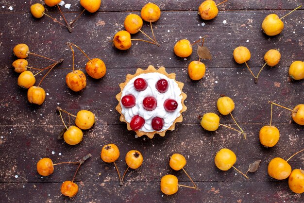 Draufsicht kleiner köstlicher Kuchen mit Hartriegel zusammen mit gelben Kirschen auf dem braunen Holztischfrucht frisch sauer weich