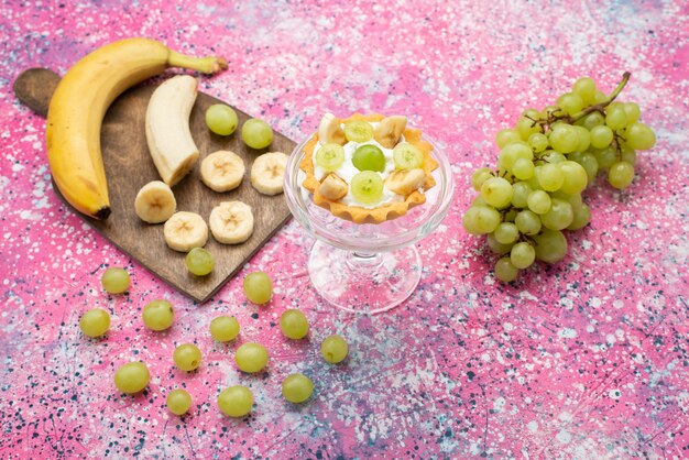 Draufsicht kleiner köstlicher Kuchen mit Sahne und geschnittenen Bananen und Trauben auf der hellen Oberfläche Frucht süß