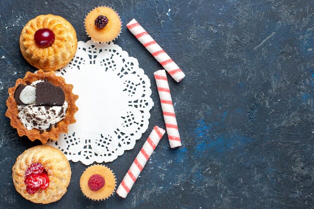 Draufsicht kleiner köstlicher Kuchen zusammen mit Keks und rosa Stockbonbonfrüchten auf dem dunklen Hintergrundkekskuchen süßes Frucht backen