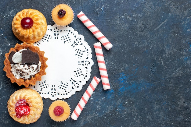 Draufsicht kleiner köstlicher Kuchen zusammen mit Keks und rosa Stockbonbonfrüchten auf dem dunklen Hintergrundkekskuchen süßes Frucht backen