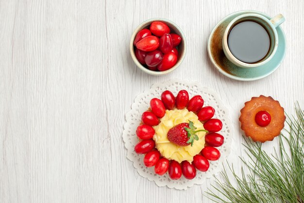 Draufsicht kleiner Kuchen mit Früchten und Tasse Tee auf weißem Schreibtisch