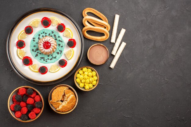 Draufsicht kleiner leckerer Kuchen mit Bonbons und Zitronenscheiben auf dunklem Hintergrund Kuchen Keks Obst Zitrus süße Kekse