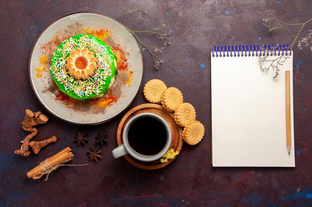 Draufsicht kleiner leckerer Kuchen mit Keksen und Tasse Tee auf dem dunklen Schreibtisch