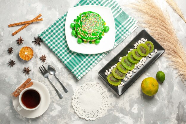 Draufsicht kleiner leckerer Kuchen mit Kiwis und Tasse Tee auf weißem Oberflächenzucker bisciut süßer Kuchen backen Sahnekeks