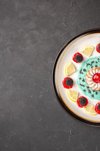 Draufsicht kleiner leckerer Kuchen mit Konfitüren und Zitronenscheiben im Teller auf dunklem Hintergrund Früchte Zitrusplätzchen Keks süß