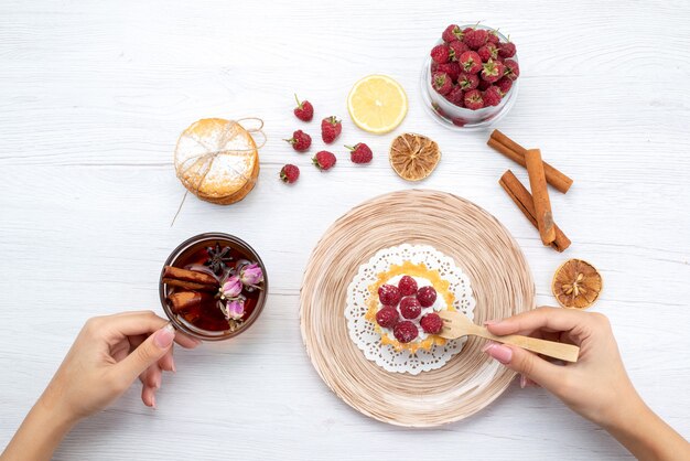 Draufsicht kleiner leckerer Kuchen mit Sahne und Himbeeren zusammen mit Sandwichkeksen Zimttee auf dem hellen Tisch Obstbeerenkuchen Keks süß