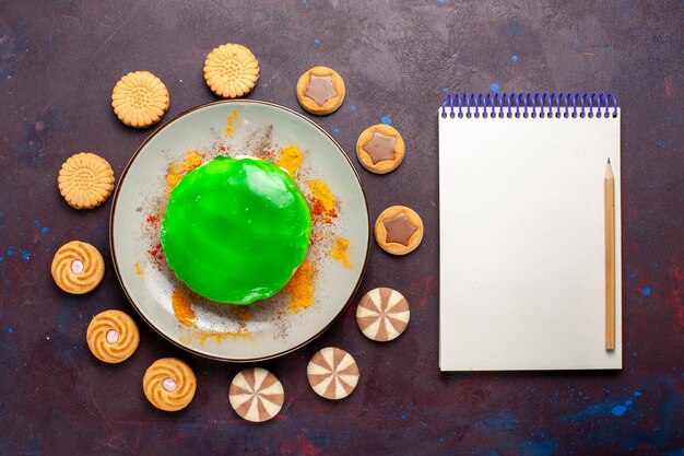 Draufsicht kleiner leckerer Kuchen mit verschiedenen Keksen auf dunklem Schreibtisch