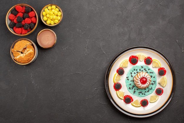 Draufsicht kleiner leckerer Kuchen mit Zitronenscheiben und süßen Konfitüren auf dunklem Hintergrund