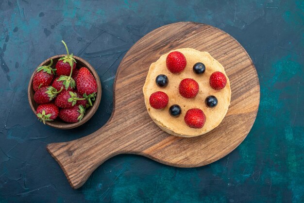 Draufsicht kleiner rund gebackener Kuchen mit frischen Erdbeeren auf der dunkelblauen Oberfläche