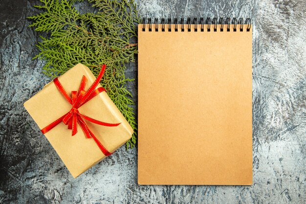 Draufsicht kleines Geschenk mit rotem Band Notizbuch Kiefernzweig auf grauem Hintergrund gebunden