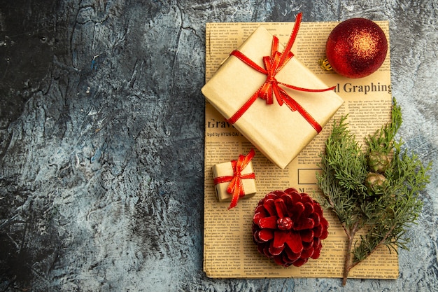Draufsicht kleines Geschenk mit rotem Band, rotem Weihnachtsball, Tannenzweig auf Zeitung auf dunkler Oberfläche gebunden