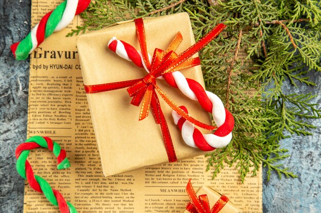 Draufsicht kleines Geschenk mit rotem Band Weihnachtsbonbons auf Zeitungskiefernzweigen auf grauer Oberfläche gebunden