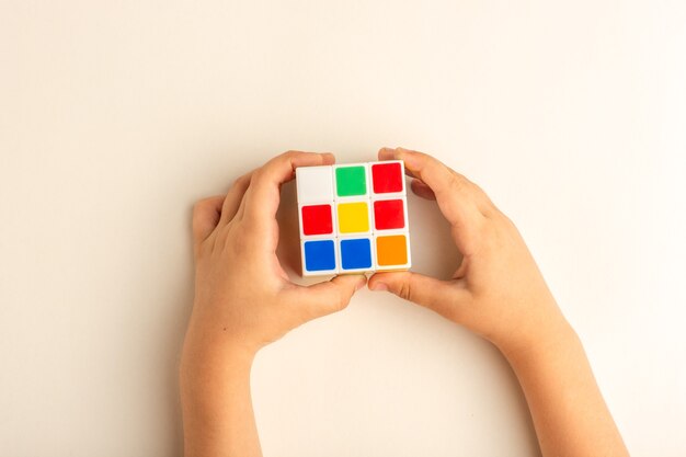 Draufsicht kleines Kind, das mit Rubikwürfel auf weißem Schreibtisch spielt