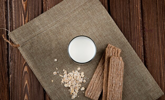 Draufsicht Knuspriges Knäckebrot mit Haferflocken und Glas Milch auf Holztisch