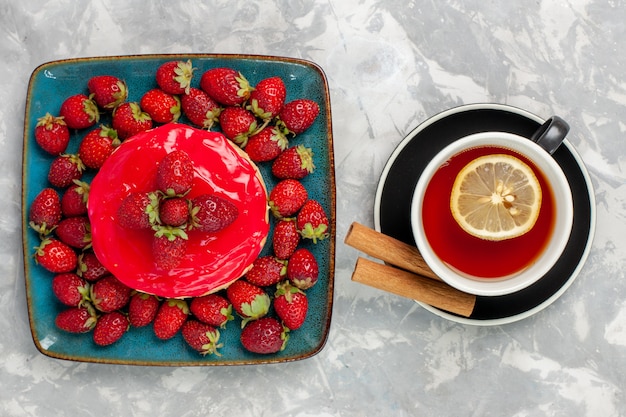 Draufsicht köstlich aussehender Kuchen kleiner Kuchen mit Tasse Tee und frischen Erdbeeren auf hellweißem Oberflächenkuchen-Keks-Kekscreme-Zuckersüß