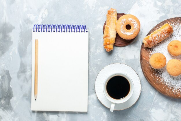 Draufsicht köstliche Bagels mit Tasse Tee und Kuchen auf hellweißem Schreibtisch.