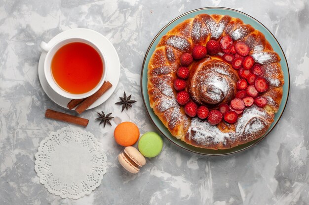 Draufsicht köstliche Erdbeerkuchen mit französischen Macarons und Tasse Tee auf weißem Schreibtischkekszuckerkuchen süßer Backkuchen