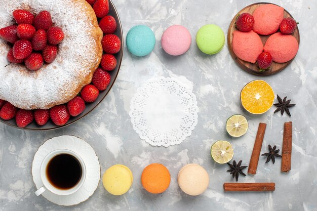 Draufsicht köstliche Erdbeerkuchen mit Macarons und Tasse Tee auf hellweiß