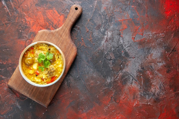 Draufsicht köstliche Fleischsuppe in kleinem Teller auf dunkelroter Oberfläche des Schneidebretts