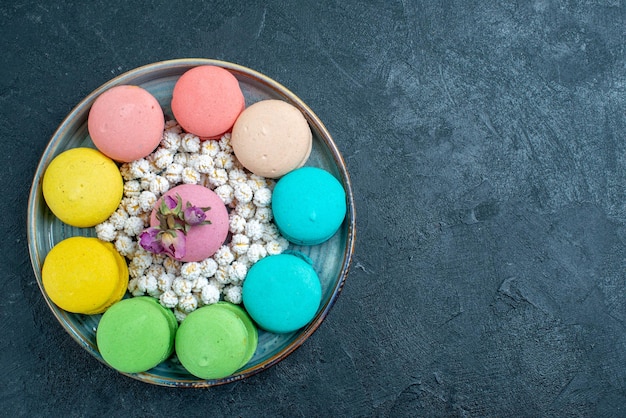 Draufsicht köstliche französische macarons mit bonbons im tablett auf dem dunklen raum