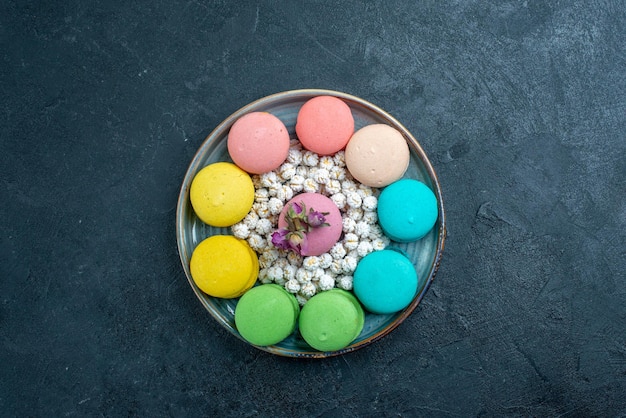 Draufsicht köstliche französische macarons mit bonbons im tablett auf dem dunklen raum