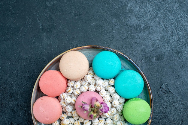 Draufsicht köstliche französische macarons mit bonbons im tablett auf dem dunklen raum