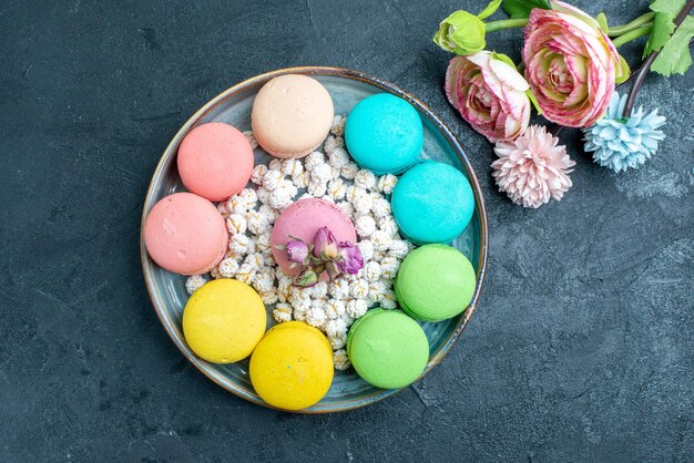 Draufsicht köstliche französische macarons mit bonbons im tablett auf dem dunklen raum