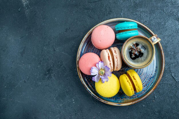 Draufsicht köstliche französische macarons mit kaffee auf dunklem raum