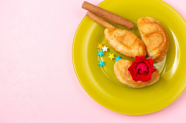 Draufsicht köstliche gebackene Croissants mit Fruchtfüllung innen mit Zimt innen grüner Platte auf dem rosa Schreibtisch