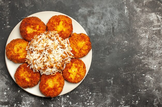 Draufsicht köstliche gebratene Schnitzel mit gekochtem Reis auf der dunklen Oberfläche Fleischgericht Fotomahlzeit