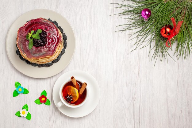 Draufsicht köstliche Gelee-Pfannkuchen mit Rosinen-fruchtigem Gelee und Tasse Tee auf hellweißem Hintergrund Marmeladenkuchen Gelee-Keks Dessert süß