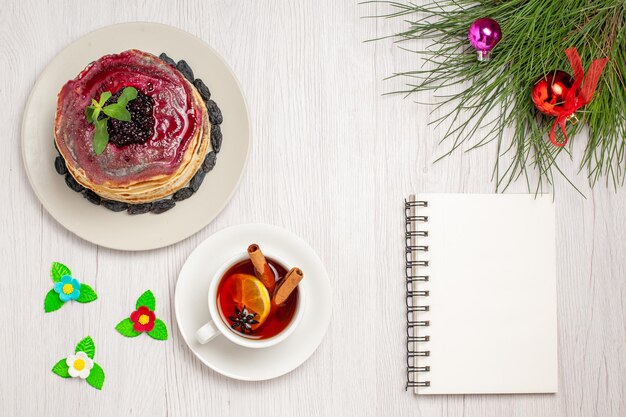 Draufsicht köstliche Gelee-Pfannkuchen mit Rosinen-fruchtigem Gelee und Tasse Tee auf weißem Hintergrund Marmelade-Kuchen-Keks-Dessert süß