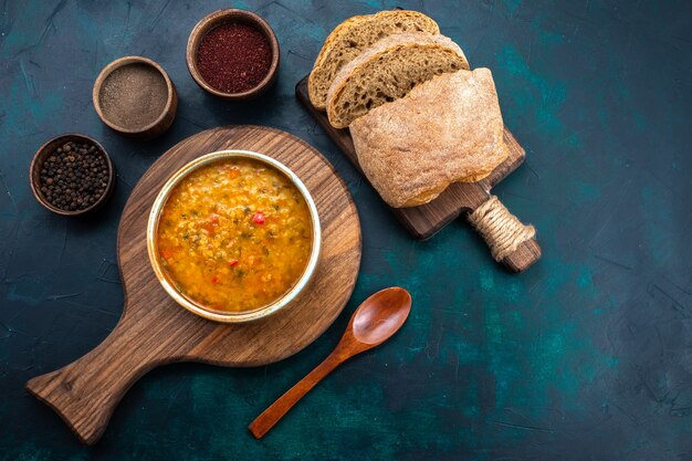 Draufsicht köstliche Gemüsesuppe in rundem Teller mit Brot und Gewürzen auf dem dunkelblauen Schreibtisch.