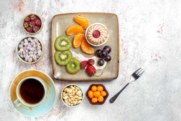 Draufsicht köstliche geschnittene Früchte mit Kuchensüßigkeiten und Tasse Tee auf weißem Hintergrund Obst frischer Tee-Süßigkeiten-Kuchen-Keks