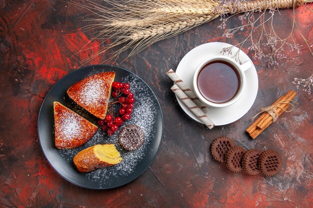 Draufsicht köstliche geschnittene Torte mit Keksen und Tasse Tee auf dunklem Tisch süßer Tortenkuchen