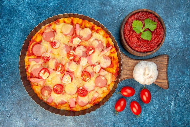 Draufsicht köstliche käsepizza mit würstchen und tomaten auf blauem hintergrund italienischer teigkuchen fast-food-fotofarbe