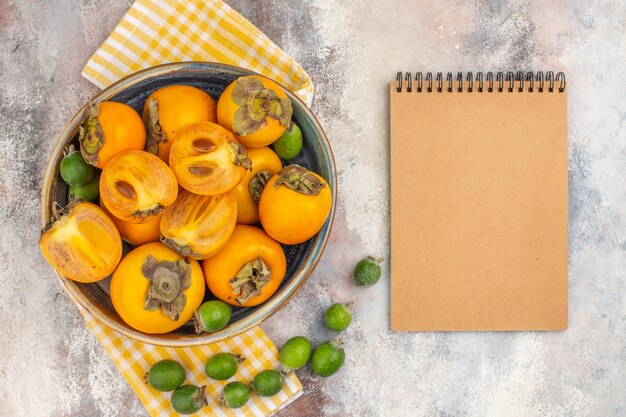 Draufsicht köstliche Kaki in einem gelben Küchentuch der Schüssel feykhoas ein Notizbuch auf nacktem Hintergrund