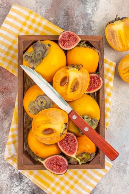 Draufsicht köstliche Kakis und geschnittene Feigen in Holzkiste gelb ein Küchentuch auf nacktem Hintergrund