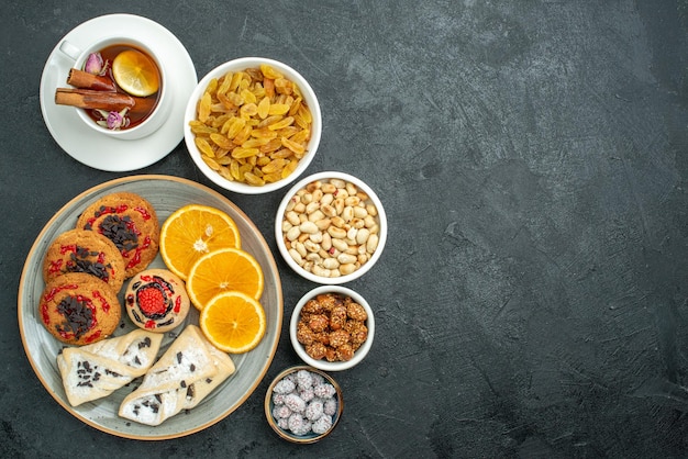 Draufsicht köstliche Kekse mit fruchtigem Gebäck Orangentee und Nüssen auf dunkler Oberfläche Nuss-Snack-Tee süße Süßigkeiten