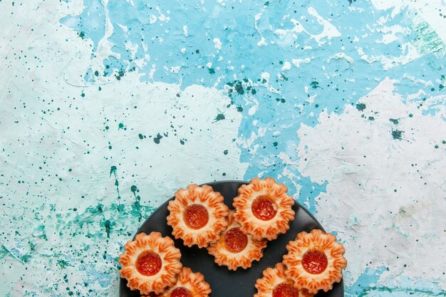Draufsicht köstliche Kekse mit Marmelade innerhalb schwarzer Platte auf hellblauem Schreibtischkekskeks süßer Zuckerfarbentee
