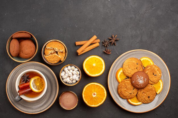 Draufsicht köstliche Kekse mit Tasse Tee und geschnittenen Orangen auf dunkler Oberfläche Zuckerkeks Dessert Keks süß