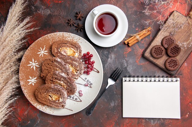 Draufsicht köstliche Keksröllchen mit Keksen und Tee auf dunklem Tisch